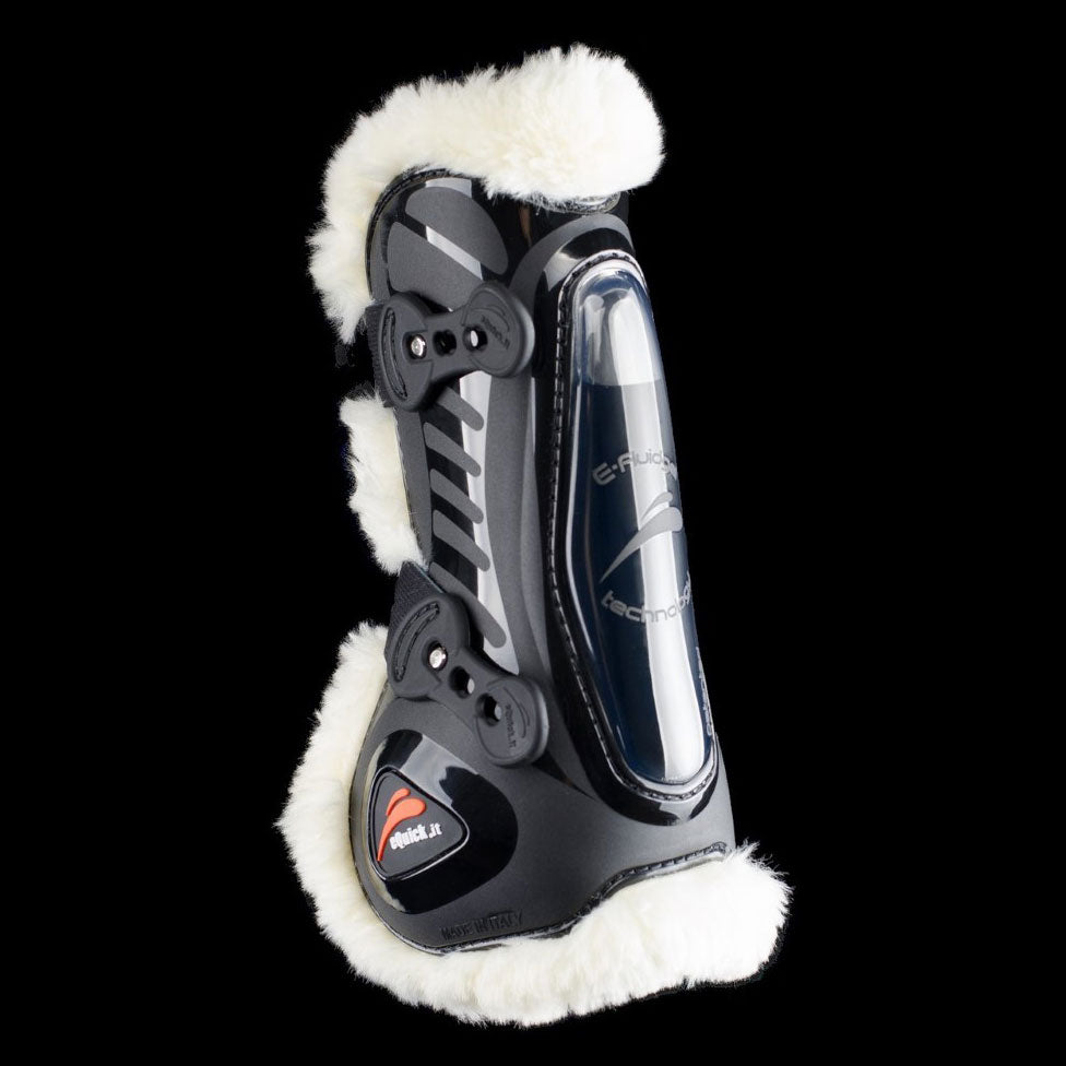 Black glossy shell front leg boot with white fluffy lining at the edges and strap closures, side view on black