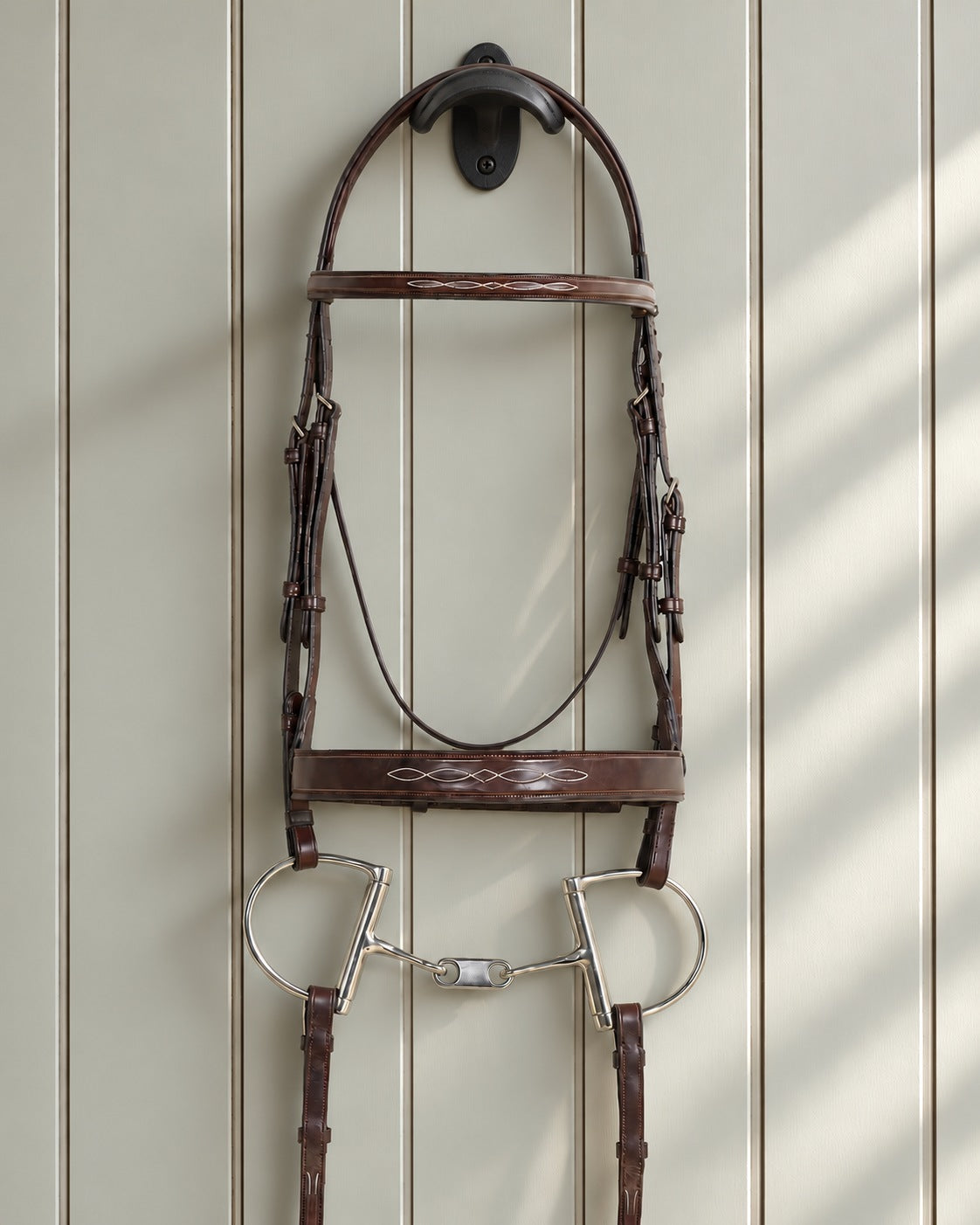 Ovation Classic wide noseband bridle with reins hung on a black cast iron bridle bracket against a grey panelled wall