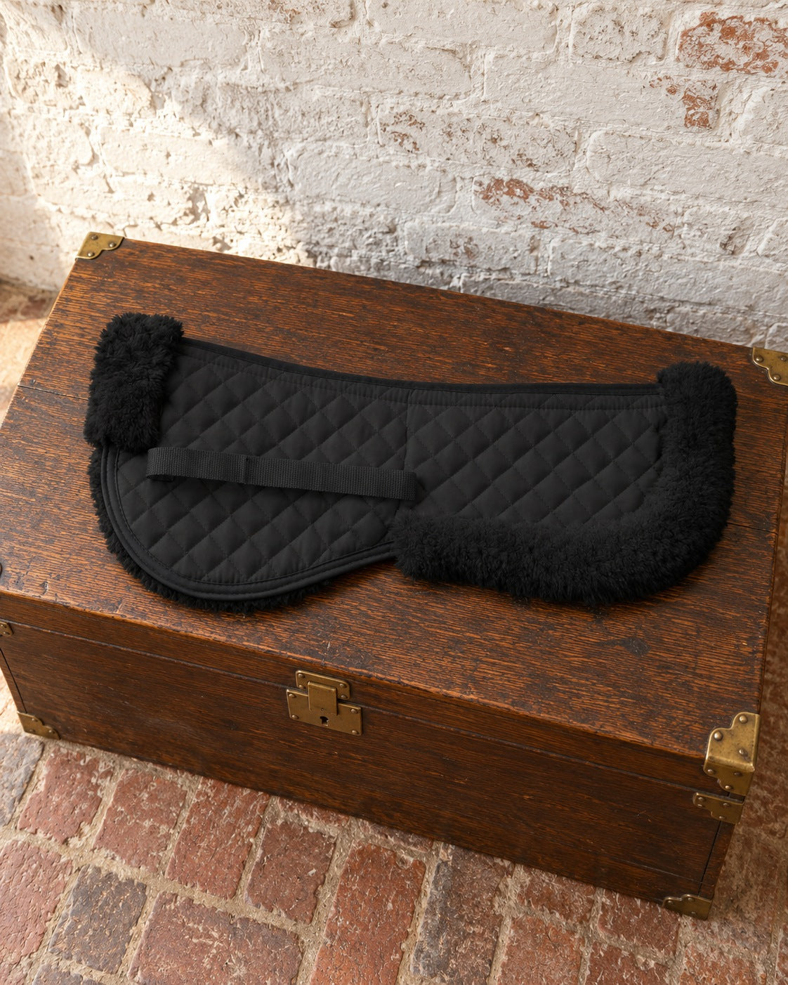 Black quilted Syntech half pad with fleece rolls on a dark oak tack trunk