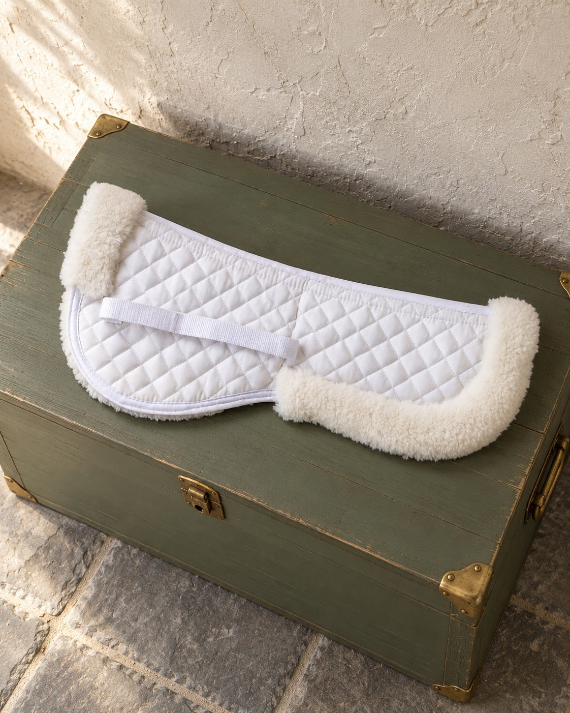 White quilted Syntech half pad with fleece rolls lying on a sage green tack trunk