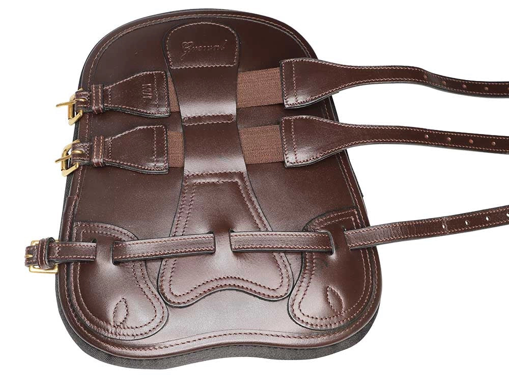 Outside of a single dark brown leather tendon boot with three straps and brass buckles, laid flat on white