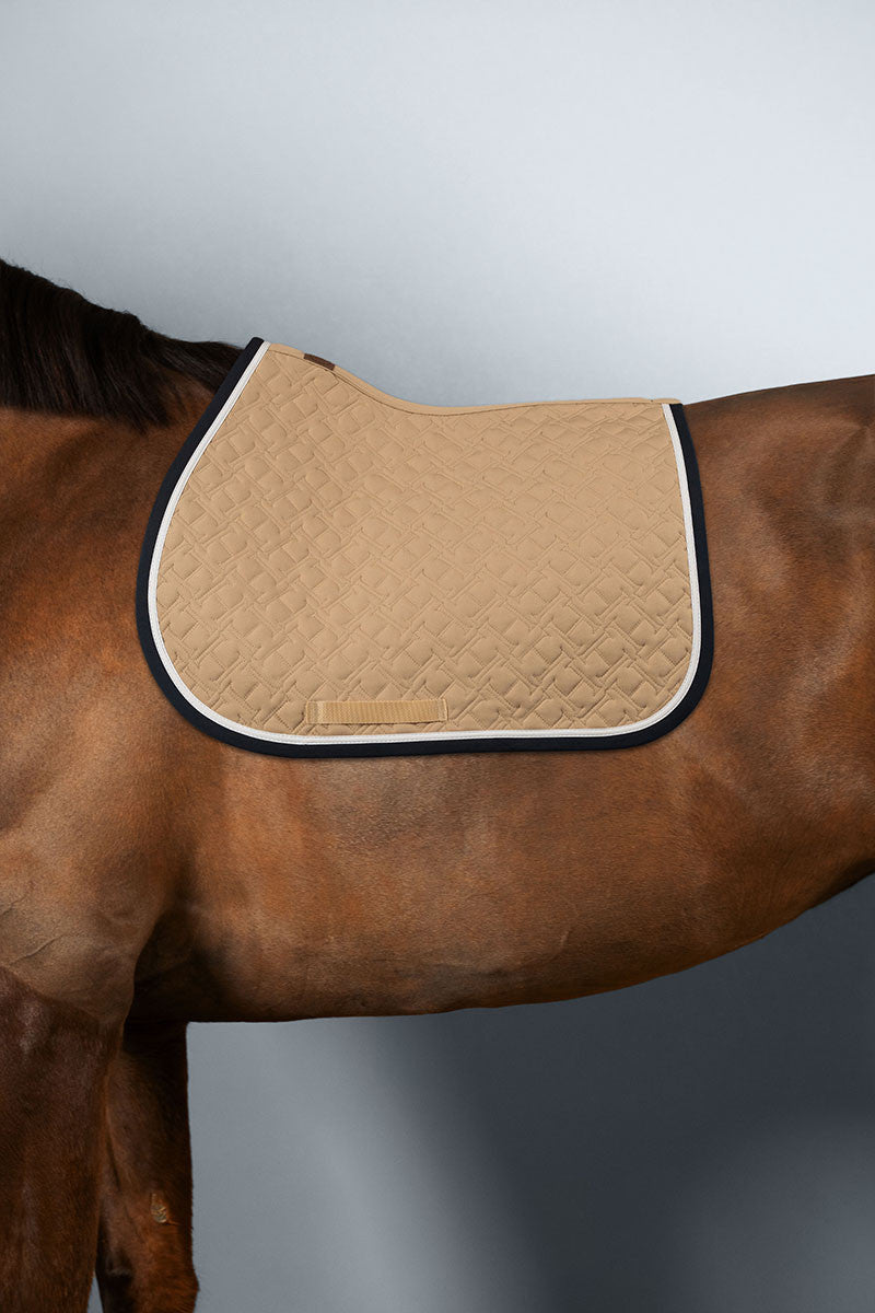 Sand quilted saddle pad with navy and white edge piping, shown on a bay horse