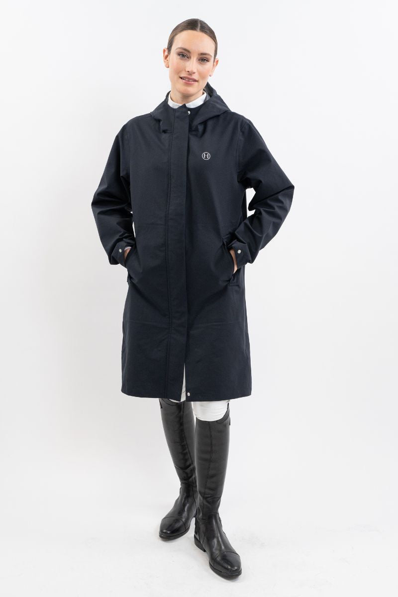 Model in the knee-length navy hooded rain coat with tall black boots, full-length front view