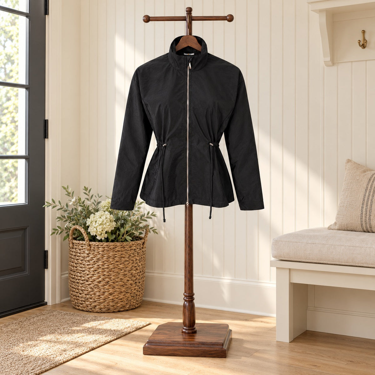 Black zip front windbreaker with a stand collar and drawstring waist on a wooden valet stand in a mudroom