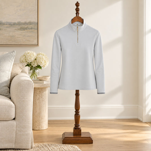Pale gray quarter zip riding shirt with long sleeves, hung on a wooden valet stand in a sitting room