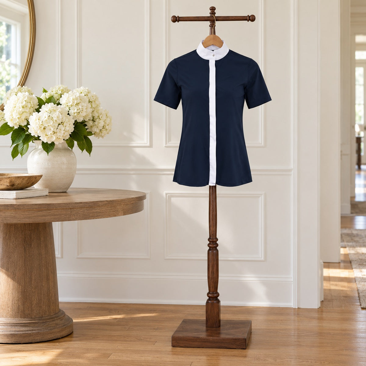 Navy short sleeve show shirt with a white collar and placket, on a wooden valet stand in an entry hall