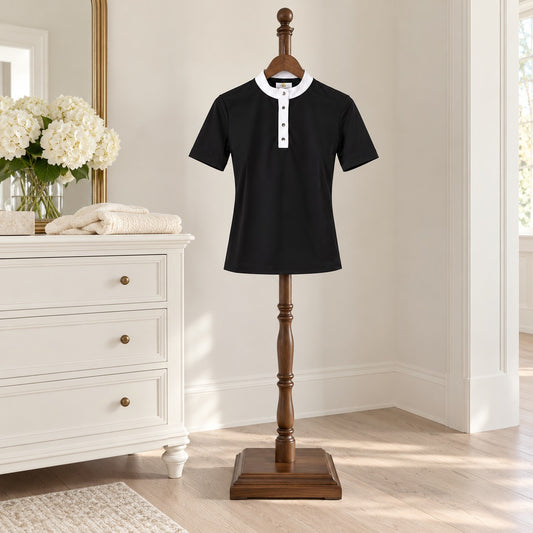 Black short sleeve riding polo with a white band collar on a wooden valet stand in a bedroom