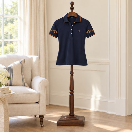 Navy short sleeve polo with cognac tipping and bit-motif sleeve embroidery, on a wooden valet stand in a sunlit room