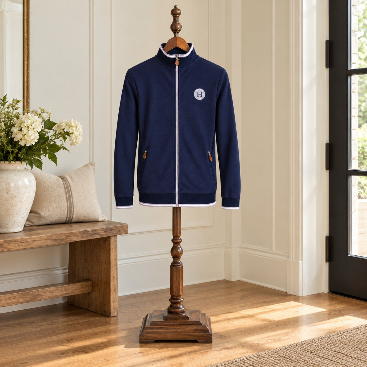 Navy zip-up sweater with a white H crest patch and contrast trim on a wooden valet stand in an entry hall
