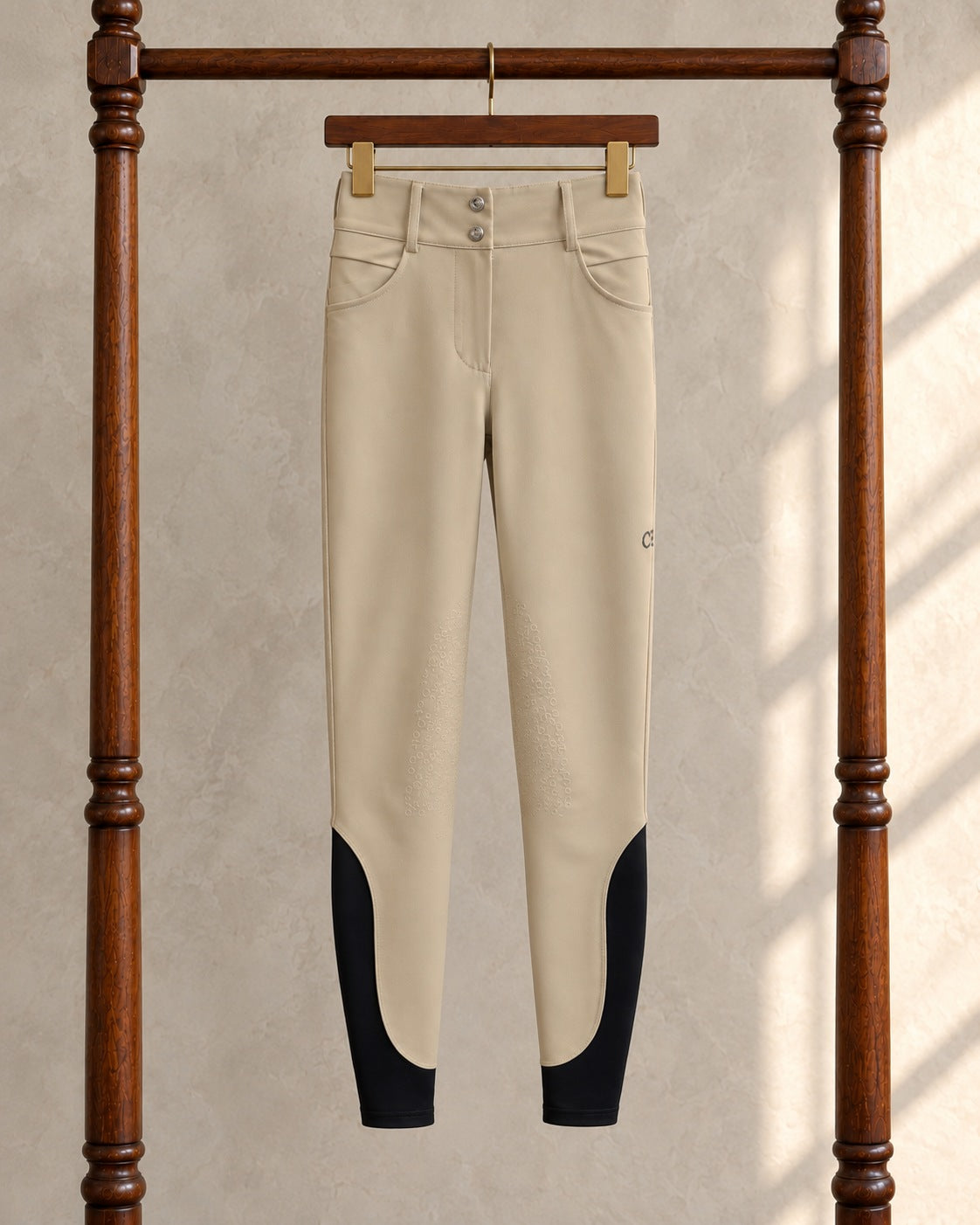 Tan American Equus performance breeches on a clip hanger on a walnut garment rack