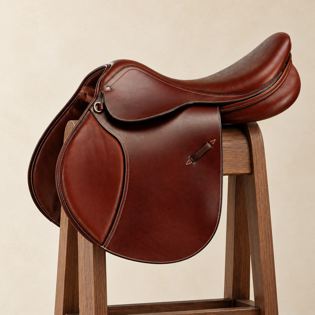 Competition Show Jumping II medium long flap close contact saddle in chestnut brown leather with a deep seat and contrast stitching, on a walnut saddle stand against a cream plaster wall