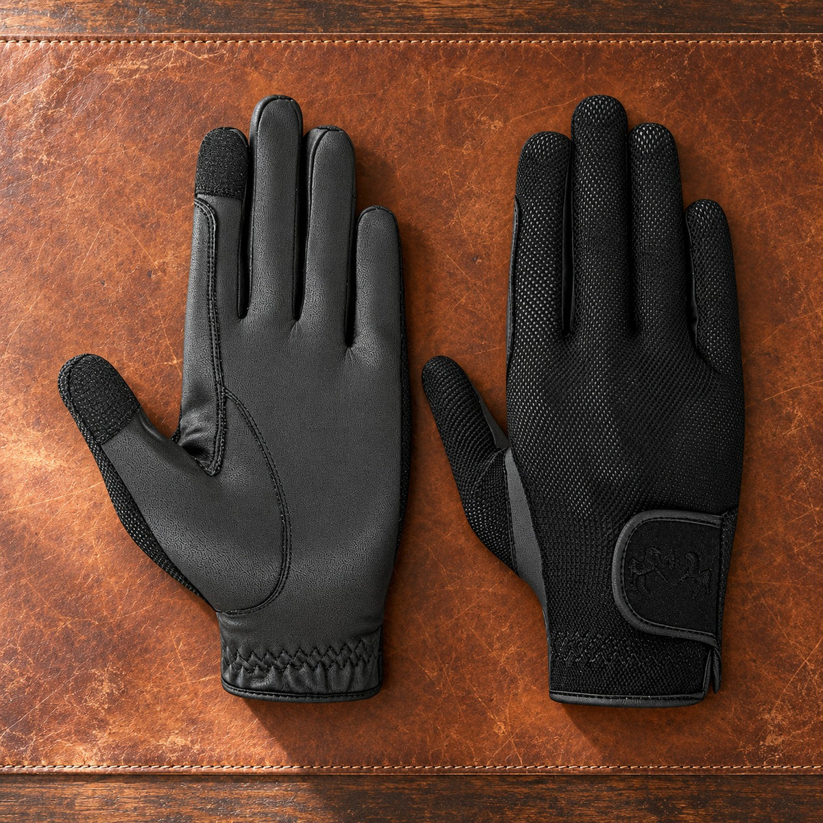 Pair of black Equine Couture Aerocool touch screen riding gloves on a cognac leather blotter