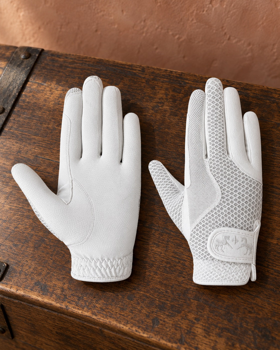 Pair of white Equine Couture Max Mesh summer riding gloves on a walnut tack trunk
