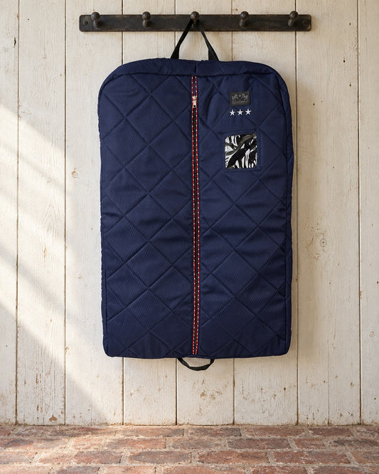 Navy quilted Equine Couture Super Star garment bag hanging from an iron peg rail on a whitewashed plank wall