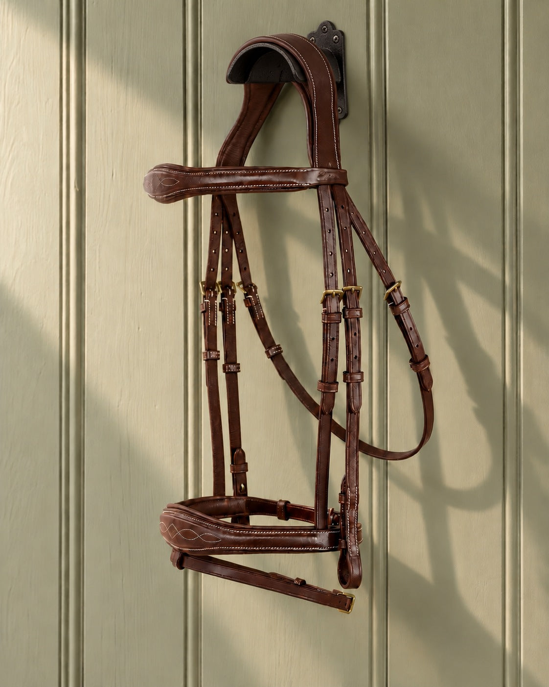 ExionPro Perseus anatomical jumping bridle hung on a black cast iron bridle bracket against a sage panelled wall