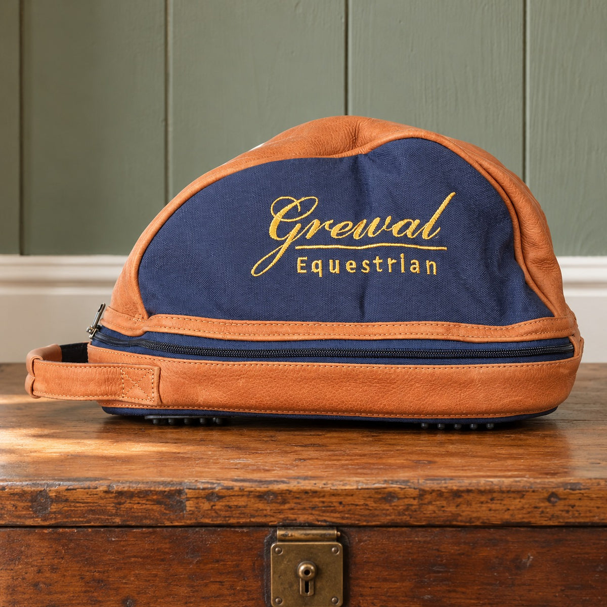 Navy Grewal helmet bag with tan leather trim on a wooden tack trunk