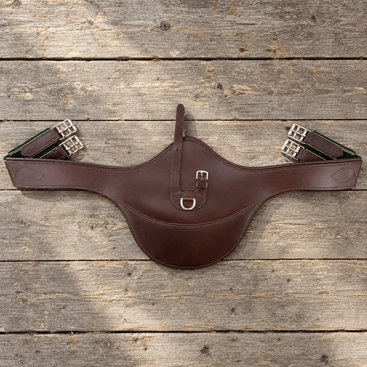 Brown leather Grewal stud guard girth lying flat on grey barn boards