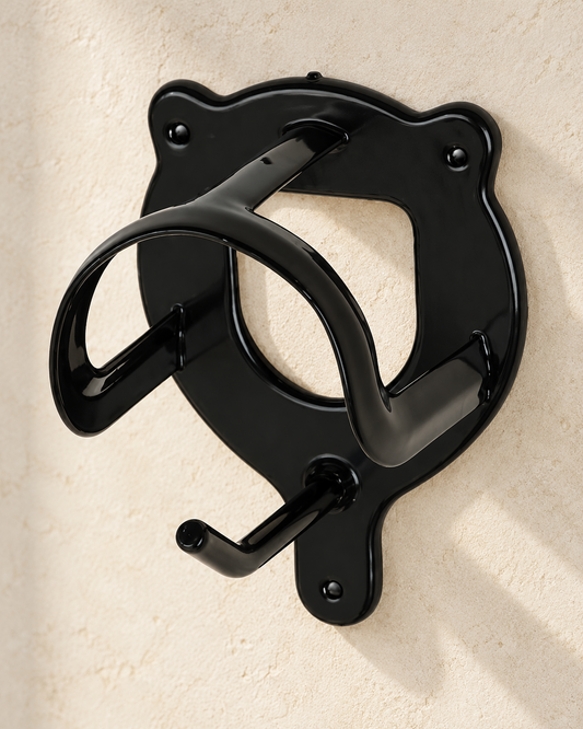 Black HDR single bridle bracket with a curved bridle hanger and lower hook, mounted on a pale stone tack room wall, three-quarter view