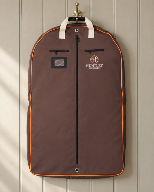 Brown Huntley Equestrian deluxe garment bag hanging from a brass coat hook on a panelled wall