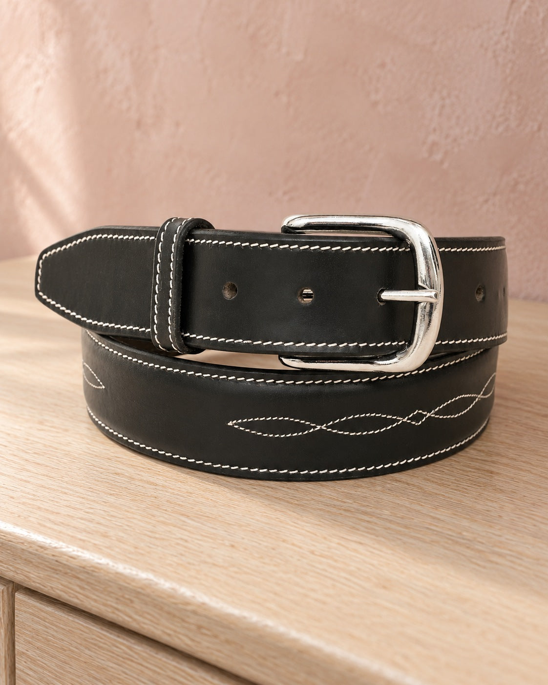 Black Huntley fancy stitched ladies leather belt with silver buckle coiled on an oak dresser