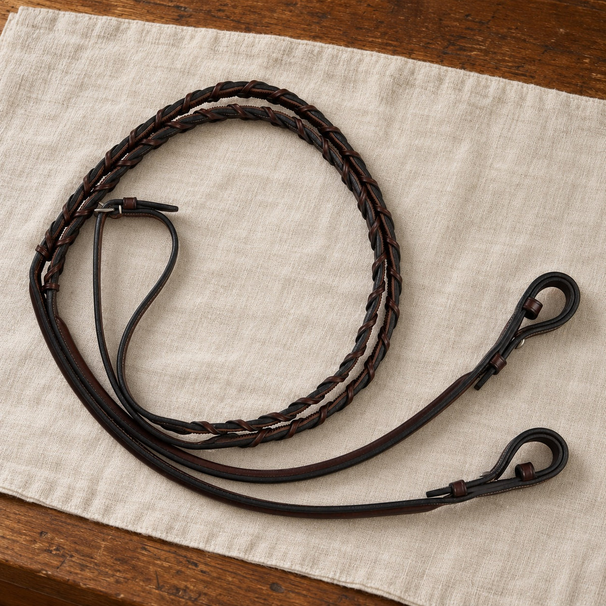Dark brown Huntley laced reins coiled on linen over a wood table
