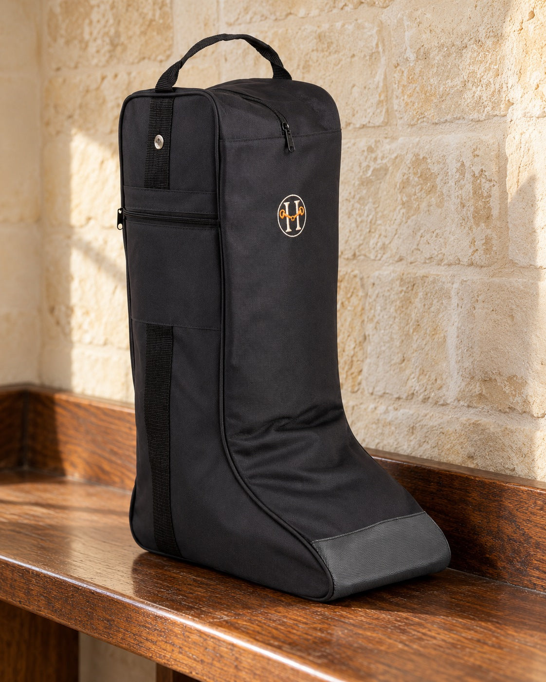 Black Huntley Equestrian tall riding boot bag on an oak bench against a limestone wall