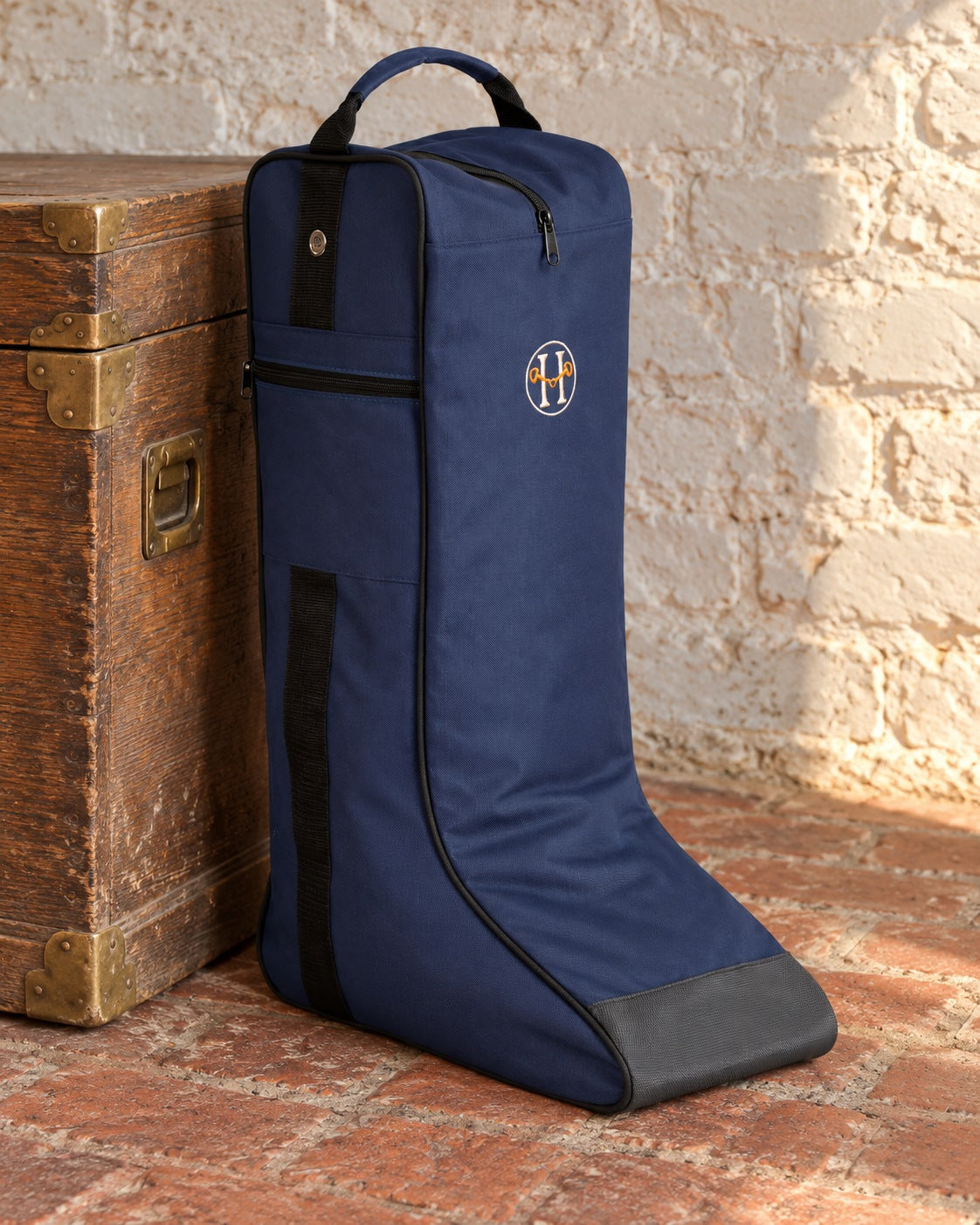 Navy Huntley Equestrian tall riding boot bag on a brick floor beside an oak trunk