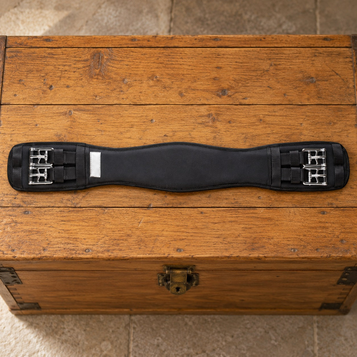 Black Lettia memory foam Clik dressage girth lying flat across an oak tack trunk
