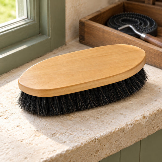 Lettia Navajo horsehair grooming brush with a plain light wood back and soft black horsehair bristles, on a limestone tack room window ledge with a wooden grooming box behind