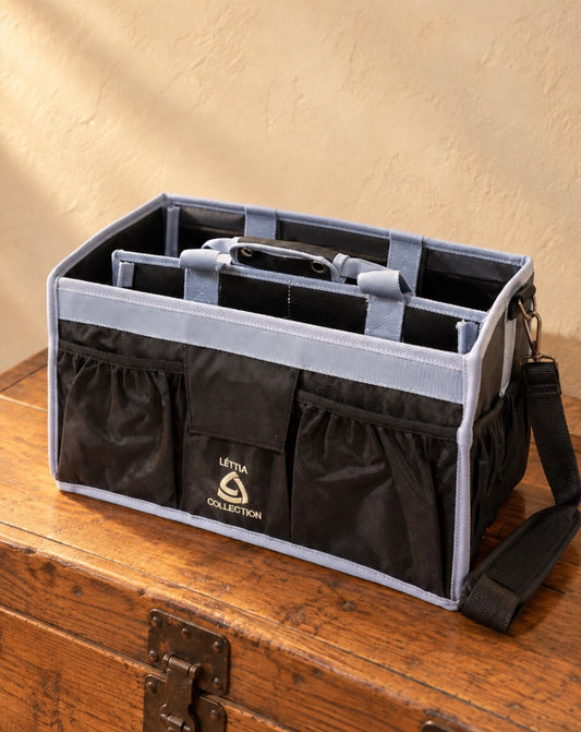 Lettia Collection grooming tote in black with grey trim, front pockets, inner handles and a shoulder strap, empty, on a wooden trunk