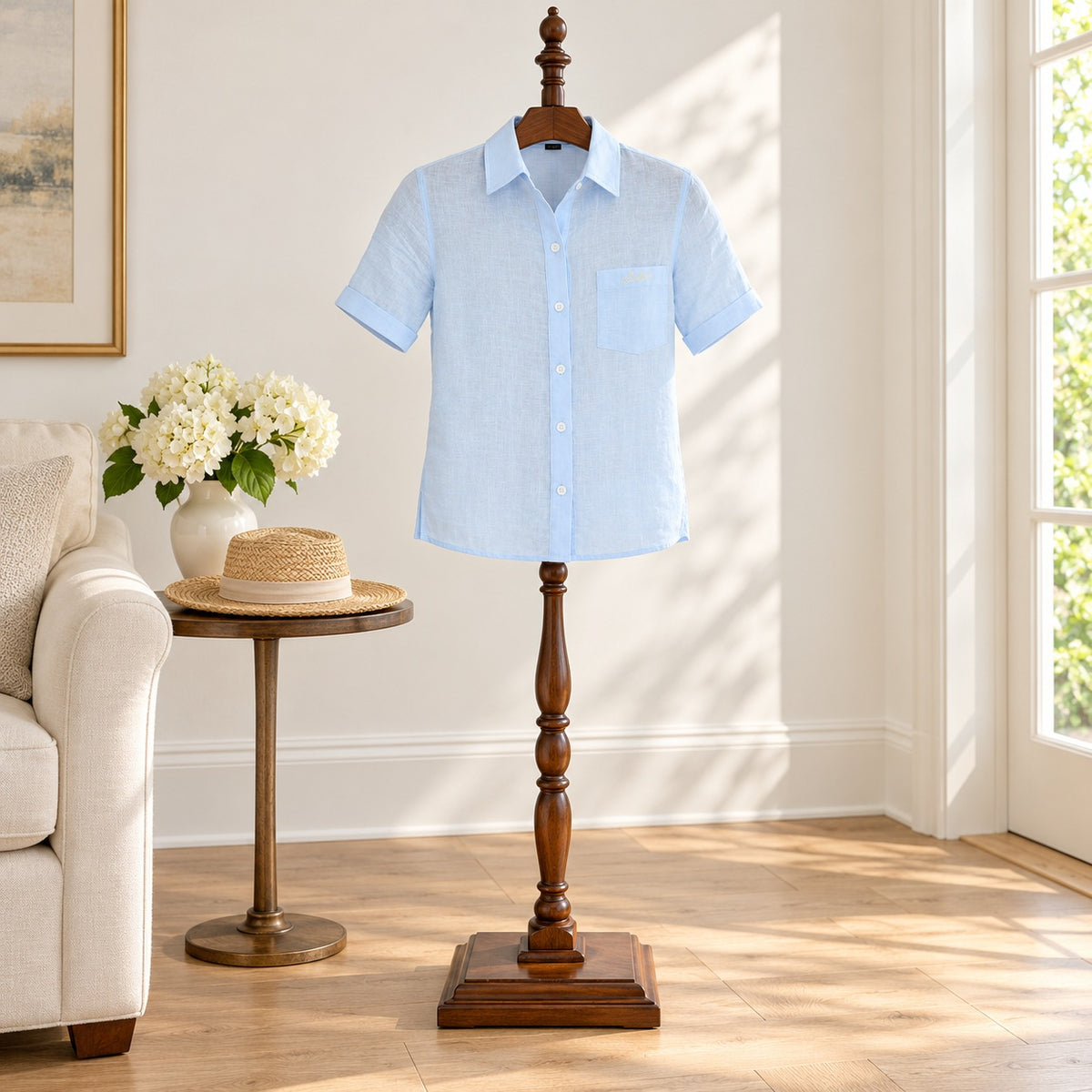Light blue short sleeve linen shirt with a chest pocket, displayed on a wooden valet stand in a sitting room