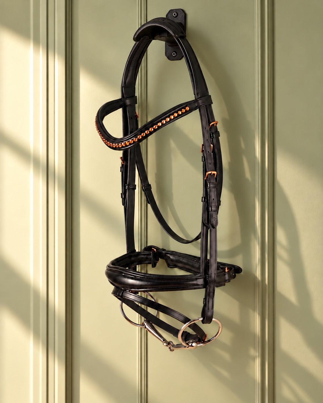 Black Munich anatomic dressage bridle with copper beaded browband hung on a black cast iron bridle bracket against a sage panelled wall
