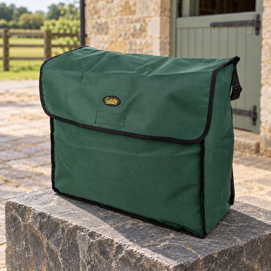 Hunter green nylon blanket storage bag with black binding, front flap and small Gatsby logo, filled and resting on a stone block in a stable yard with a limestone wall and sage half-door behind