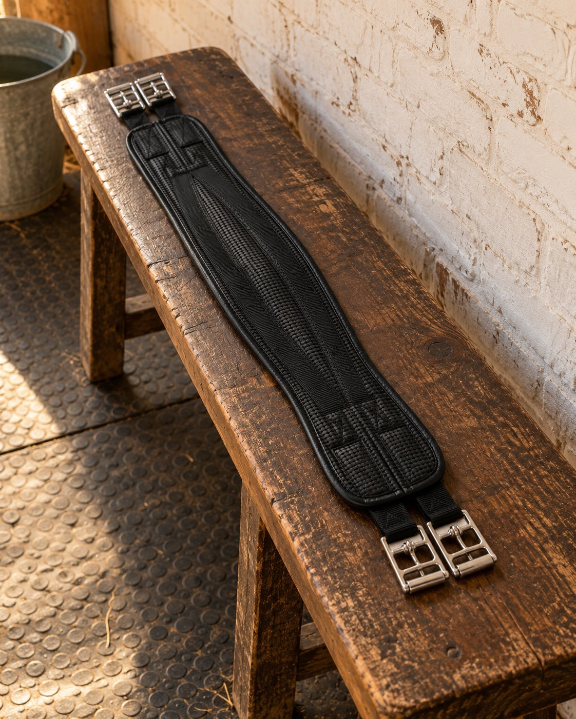 Black Airform all-purpose chafeless girth on an oak bench against a whitewashed brick tack room wall