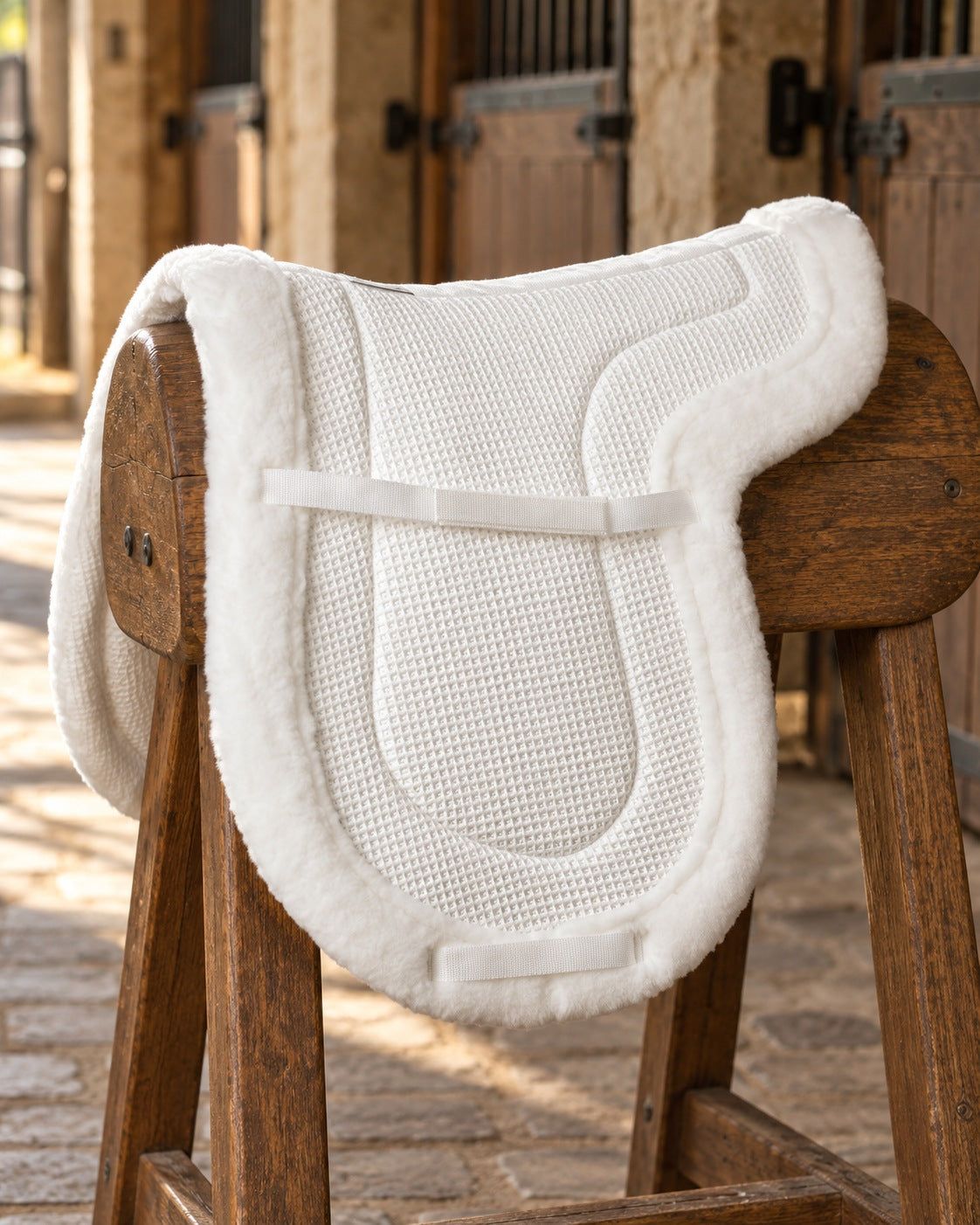 White Ovation Airflow hunter saddle pad with fleece edge draped over a wooden saddle horse in a barn aisle