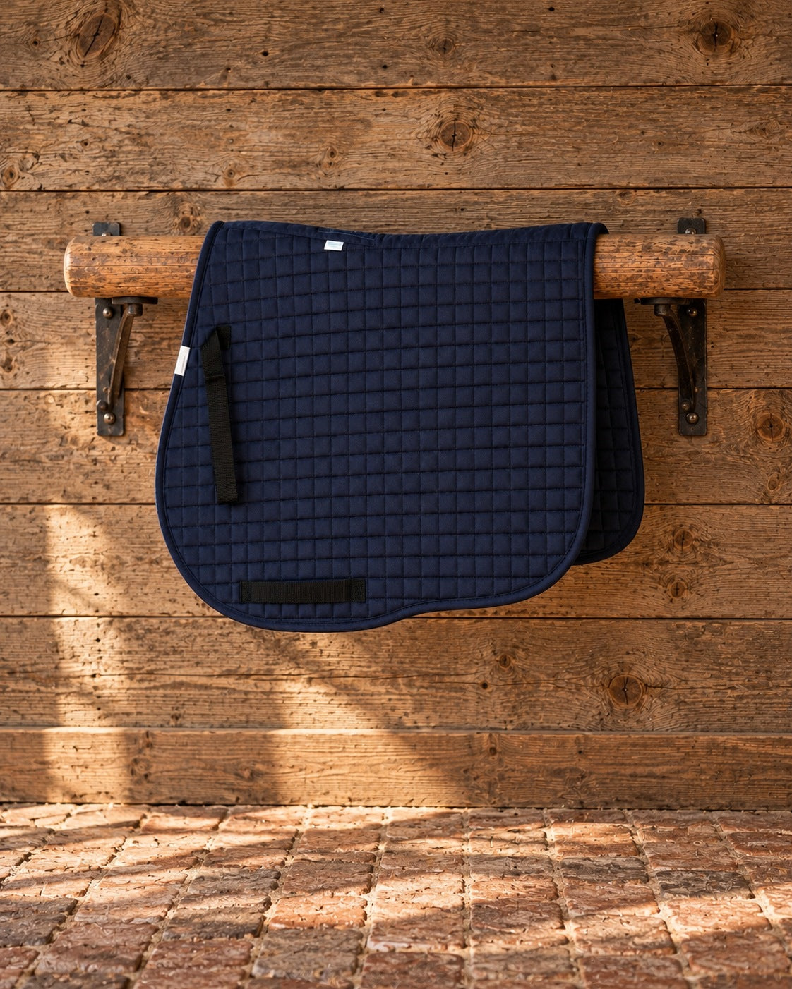 Navy Coolmax jumper saddle pad on a wooden rail against a weathered wood wall