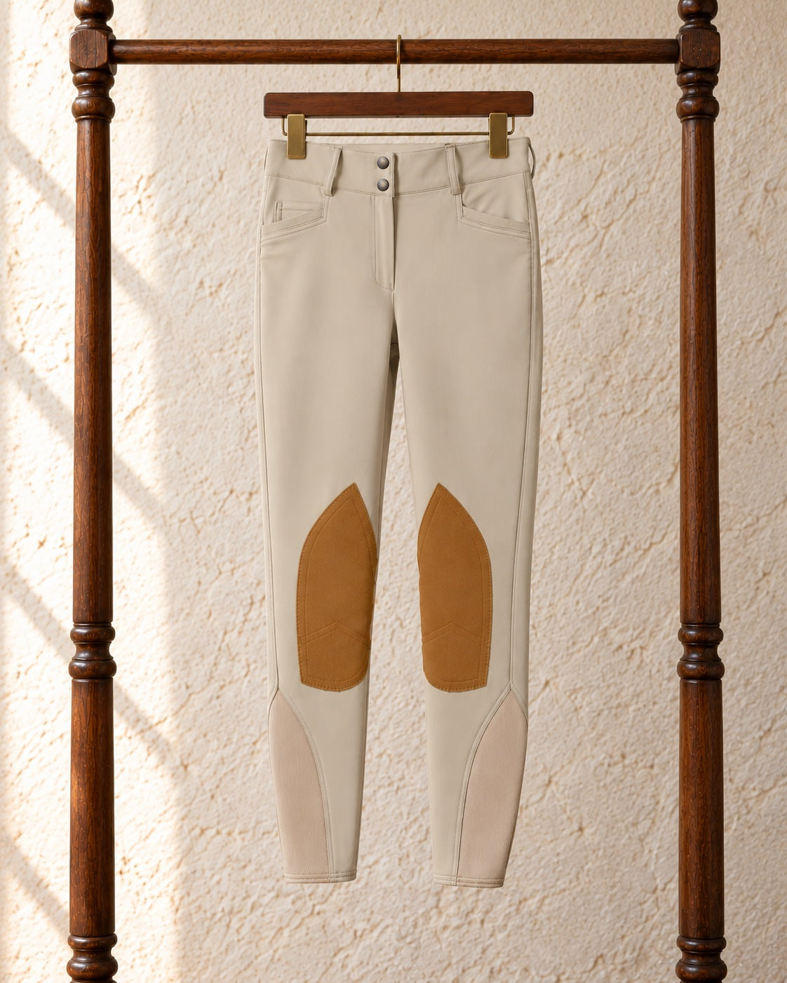 Tan Ovation Dynamic hunter breeches with suede knee patches on a wooden clip hanger on a walnut garment rack