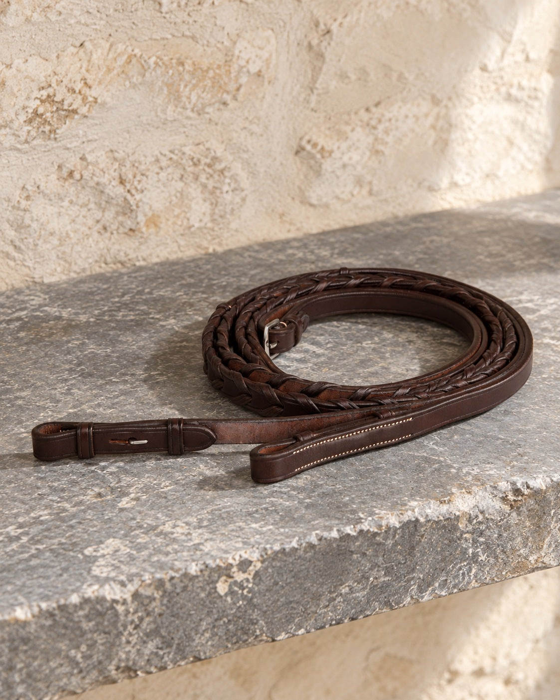Dark brown Ovation Elite laced leather reins coiled on a slate shelf