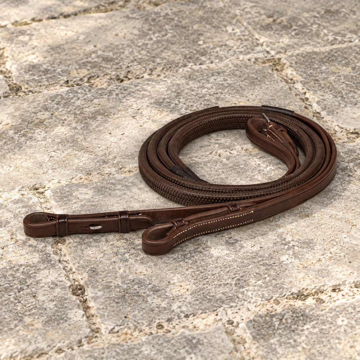 Brown Ovation Elite rubber grip reins coiled on stone flags