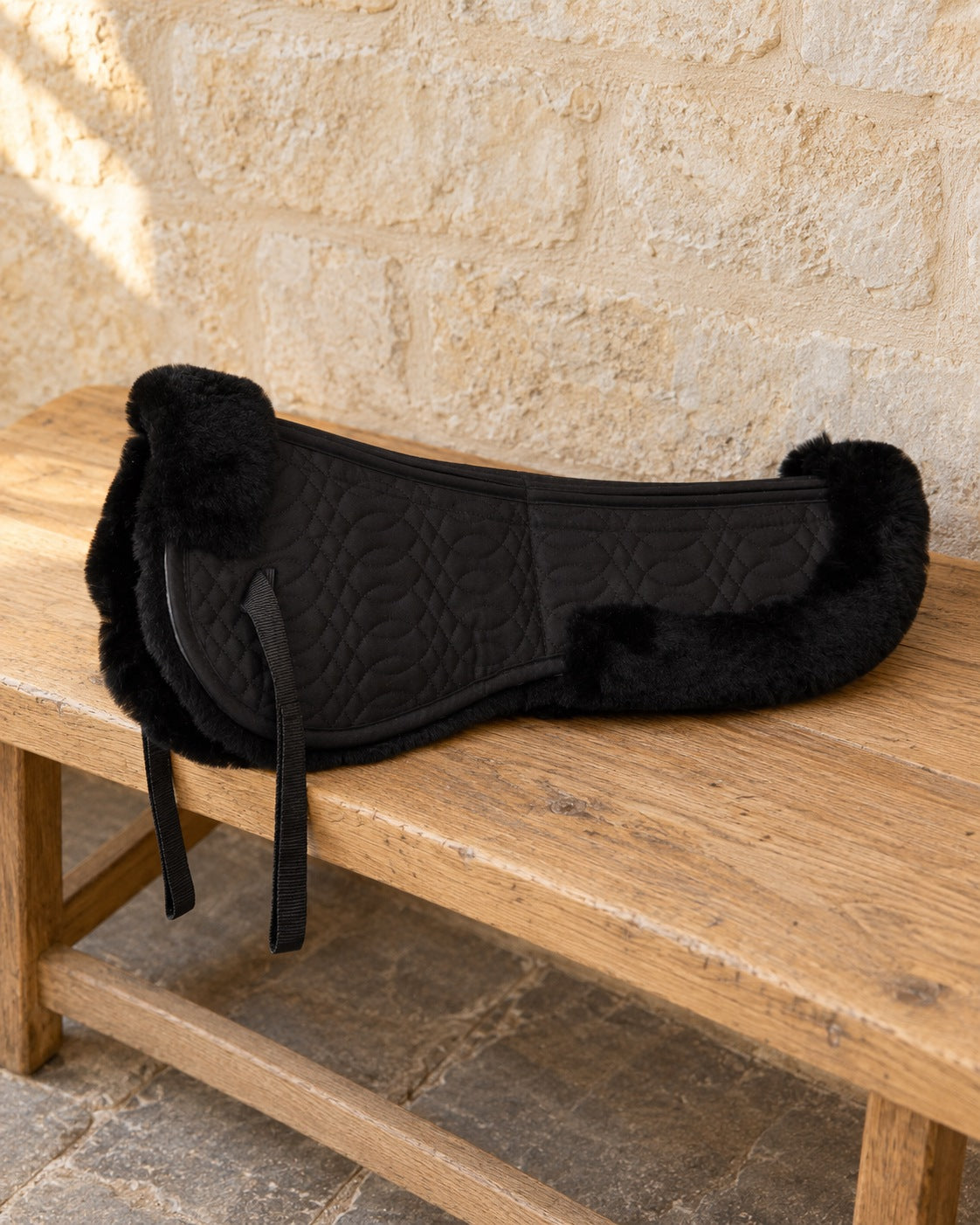 Black Europa sheepskin half pad on an oak bench against a limestone wall