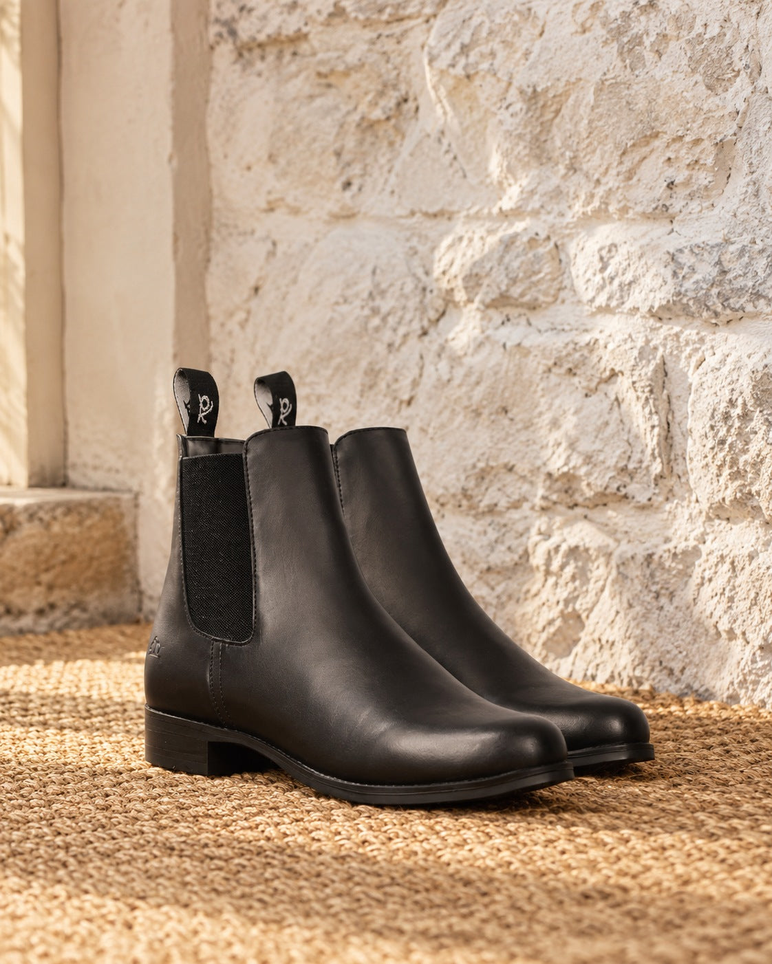 Pair of black Ovation Finalist jodhpur boots on a sisal mat against a whitewashed stone wall