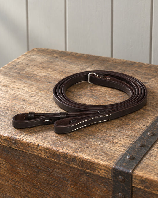 Dark brown Ovation flat leather reins coiled on an oak tack trunk