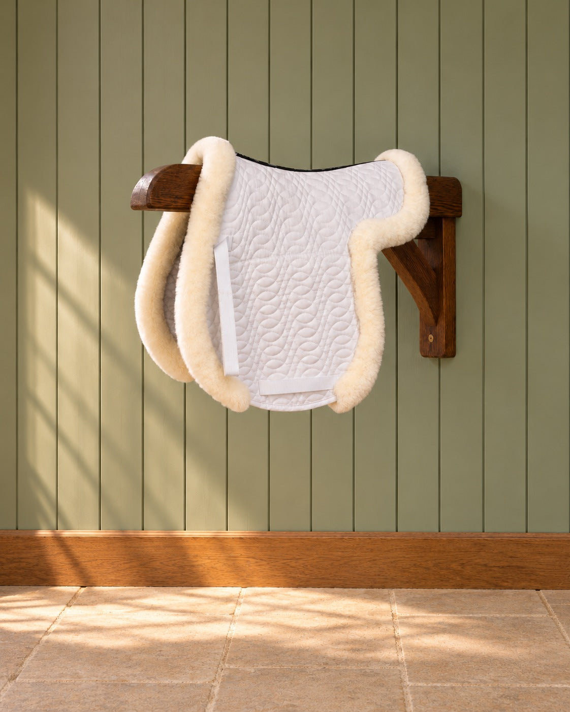 White Ovation hunter contoured saddle pad with channel spine on a wooden wall bracket against a green panelled wall