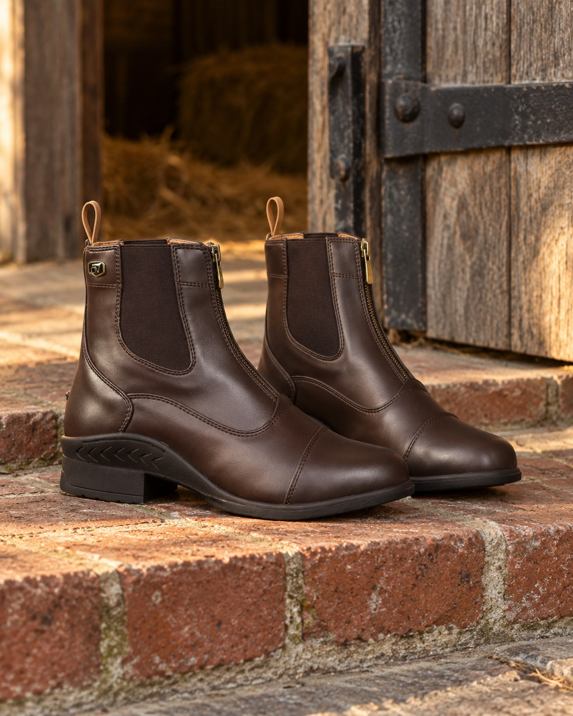 Pair of dark brown Ovation Quantum zip paddock boots on a worn brick step at a stable doorway