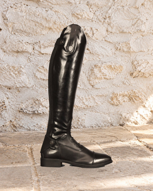 Black Ovation Sofia Grip tall riding boot in side profile on a limestone floor against a whitewashed stone wall