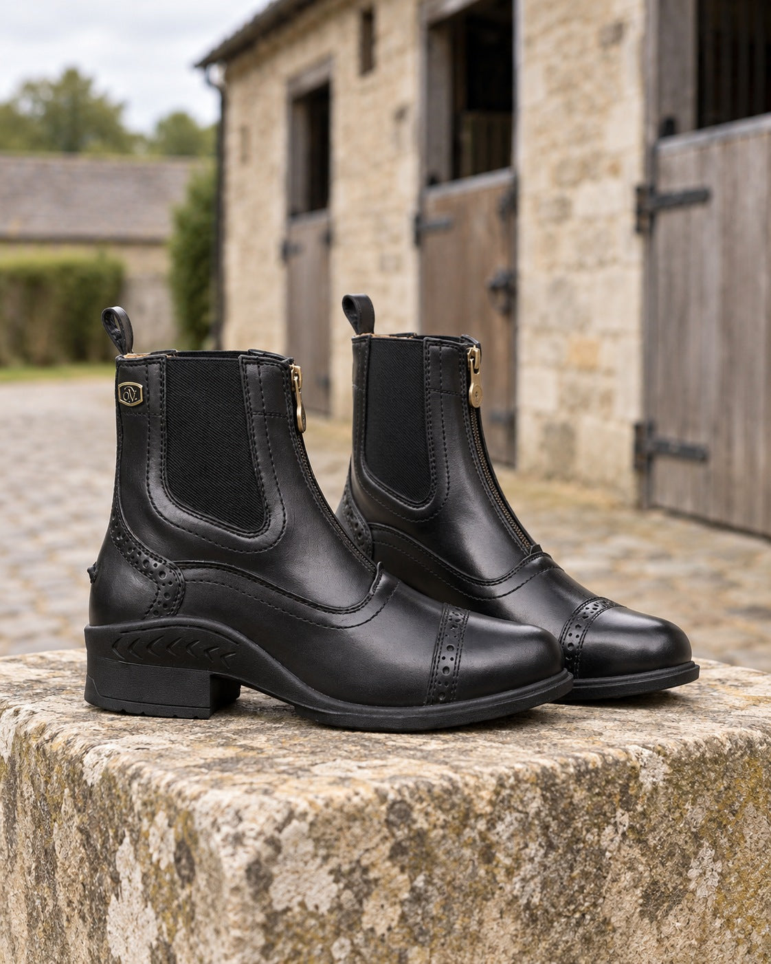 Pair of black Ovation Tuscany zip paddock boots with brogue detail on a limestone mounting block in a stable yard