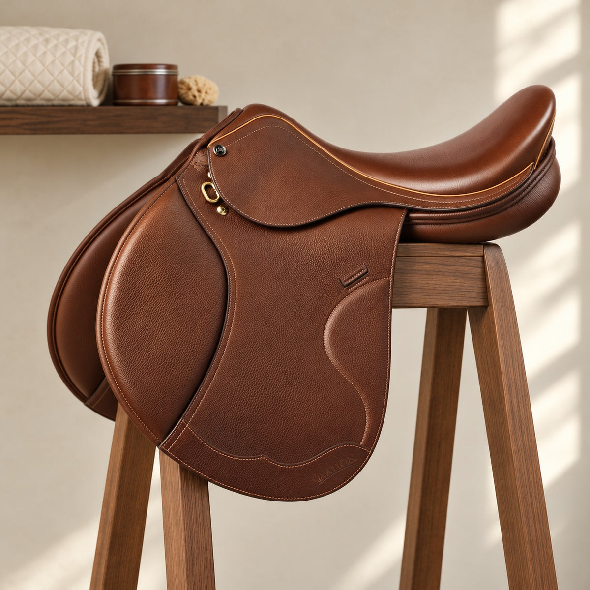Palermo II close contact saddle in tan pebbled leather with a brass dee and gold piping, on a walnut saddle stand in a tack room, quilted pad and leather care tin on a shelf