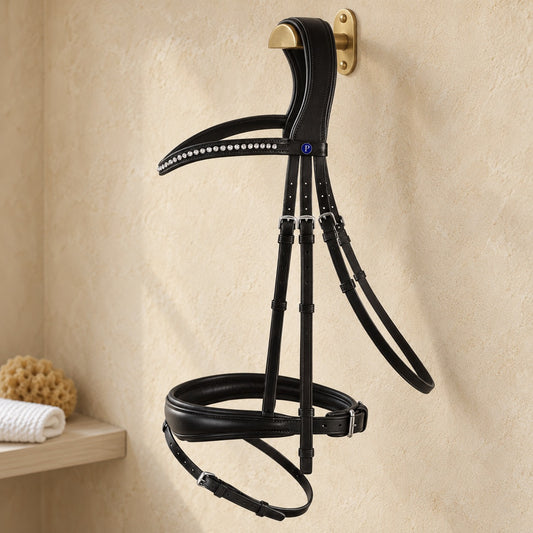 Passier Blu Spirit snaffle bridle in black leather with a crystal browband and blue P badge, hanging from a brass bridle hook on a warm sandstone plaster tack room wall