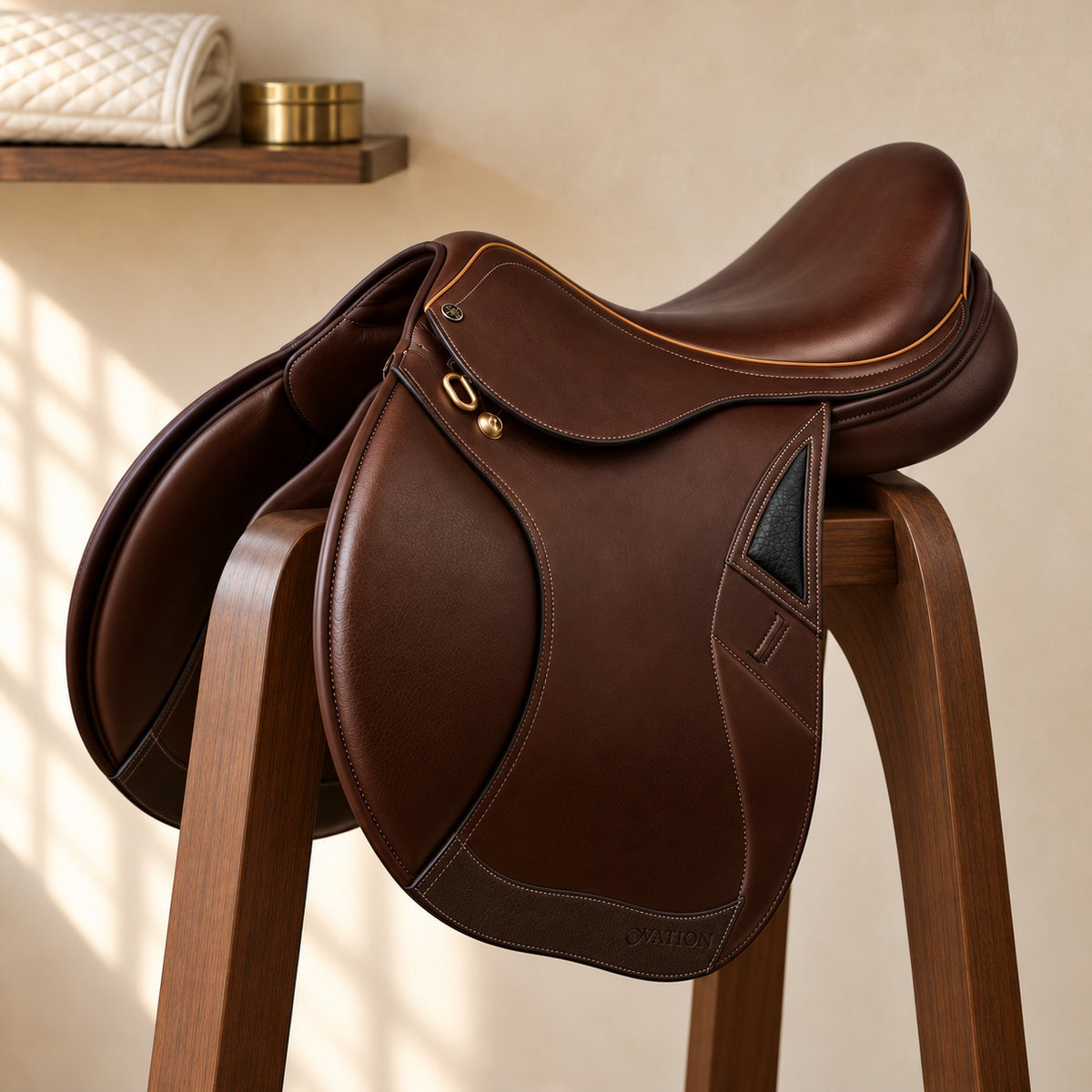 San Diego II close contact saddle in dark chocolate leather with tan piping, a brass dee and a black pebbled thigh-block insert, on a walnut saddle stand in a warm plaster tack room