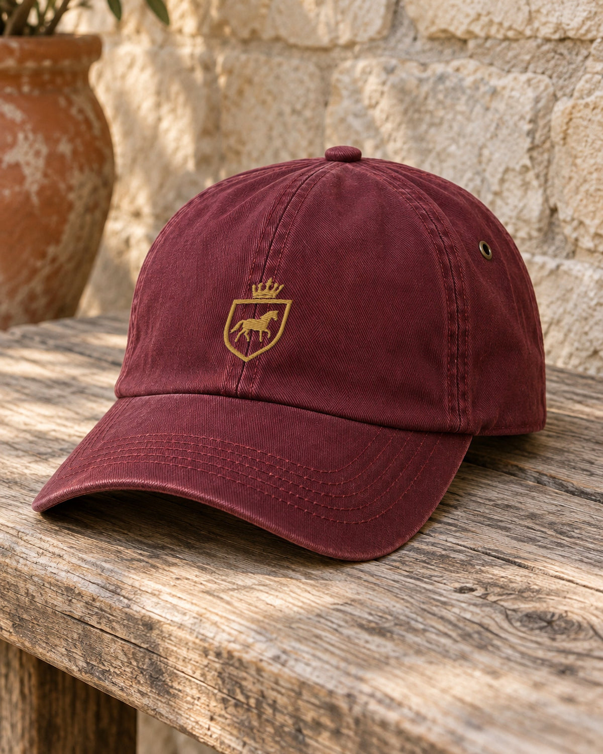 Canter & Crest Signature Crest Cotton Cap in Maroon, gold embroidered Signature crest on the front panel, on a weathered timber bench